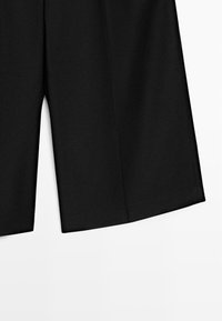 Pantaloni neri a gamba larga con una spacco centrale frontale, mostrati su uno sfondo bianco neutro.