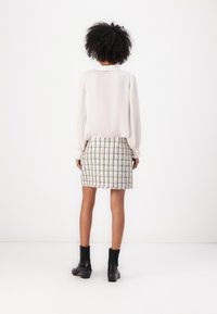 White blouse with pleated sleeves, paired with a multicolor tweed skirt. Black heeled ankle boots with ribbed cuffs. Plain white background.