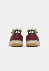 Røde og hvite sneakers laget av semsket skinn og lær, med en beige såle, sort hælhette med hvit 'VEJA'-logo og polstret krage.