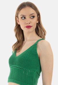 Zöld kötött crop top V-nyakkal és vékony pántokkal. Részletes textúrájú mintázattal és testhez álló fazonnal rendelkezik. Könnyű anyagból készült.