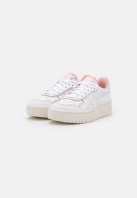 White low-top sneakers with pink accents, smooth leather texture, perforated detailing, and thick beige rubber sole. Laces and padded collar.