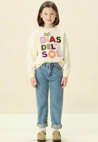 Sweatshirt crème avec le texte coloré "Días del Sol", associé à un jean bleu clair orné de petits cœurs dorés brodés et d'un ourlet retroussé.