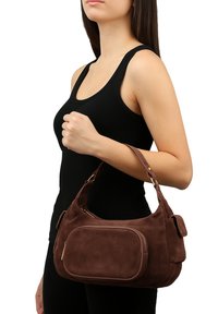 Borsa in suede marrone con forma curva e bordi arrotondati, dotata di una tasca frontale e di una tracolla removibile.