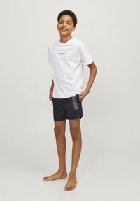 Camiseta de algodón blanca con el texto "Original Studio". Pantalones cortos de baño azul oscuro con un patrón espiral blanco, corte relajado y bolsillos laterales.