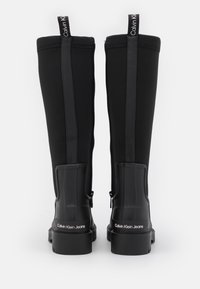 Sorte knæhøje støvler lavet af vandafvisende materiale med en glat, blank plastikdetalje, lynlåslukning og mærkevarehældetalje.