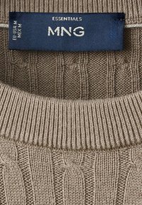 Étiquette de vêtement bleue sur un vêtement en maille beige indiquant la marque MNG Essentials et la taille EU USA M MEX M.