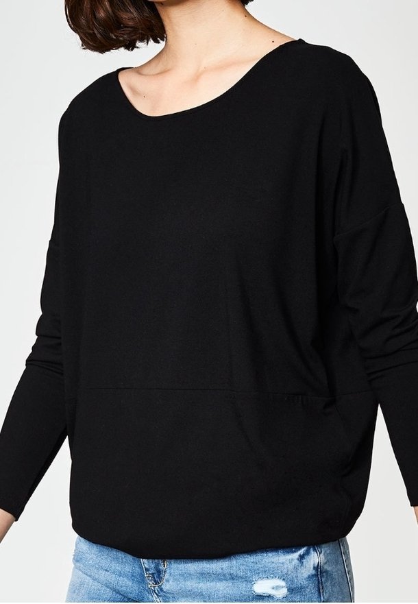 Svart långärmad topp med en vid rundad hals och avslappnad passform, gjord av mjukt tyg; bärs med ljusblå slitna jeans.