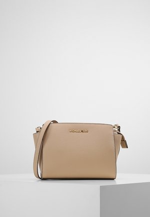 Beige Michael Kors handtas met een crossbodyriem, gestructureerde silhouet en gouden logo aan de voorkant, geplaatst op een witte ondergrond.