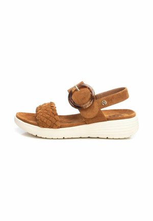 Sandal de ante marrón con una tira trenzada y una hebilla circular de acrílico, con una suela blanca ligera para mayor comodidad.