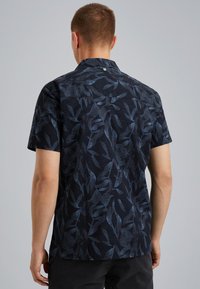 Camisa de manga corta en azul marino oscuro con un patrón de hojas. Fabricada en tejido texturizado, presenta un collar puntiagudo y un dobladillo recto.