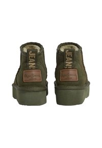 Botas de ante verdes hasta el tobillo con forro de piel sintética, costuras reforzadas y un parche de cuero marrón con el logo en el talón. Suela de goma plana.