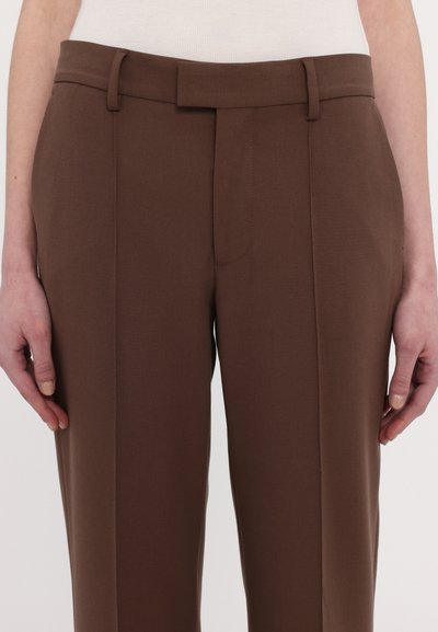 Pantalons tailleurs marron avec une texture lisse, présentant un devant plat, des passants de ceinture et des coutures latérales. Design classique pour les tenues formelles.