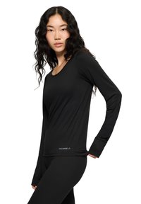 Czarna koszulka z długim rękawem, uszyta z gładkiego materiału, z dekoltem w kształcie łódki. Posiada logo Merrell na dolnym szwie. Dopasowany krój przeznaczony do aktywności.