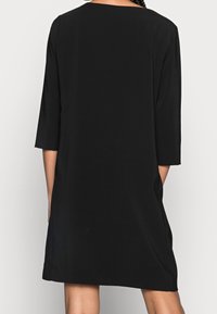 Vestido negro de longitud a la rodilla con mangas tres cuartos, escote redondo y corte recto, hecho de una tela suave, con aberturas laterales.