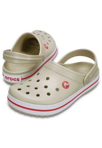 Beige plastic clogs with ventilation holes, back strap, red and white accents, and a circular logo on the side.