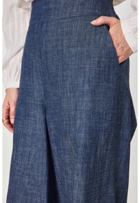 Pantaloni in denim con vita alta e tasche laterali, realizzati in un tessuto testurizzato di un blu scuro e con un taglio a gamba larga.