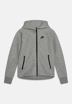 Giacca con cappuccio Nike grigia con zip frontale, maniche raglan, due tasche con zip nere e un logo nero sul petto. Tessuto morbido e texture.