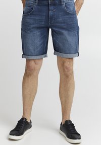 Tumši zila denim šorti ar salocītām malām un priekšējām kabatām. Apvienoti ar melniem ādas čībām.