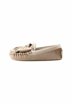 Beige sutsko med en blød, struktureret overdel og sløjfedesign; har en rund tå, syede detaljer og en flad gummisål.