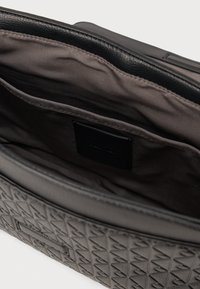 Fekete, textúrás táska geometriai mintával, sötét szövetbéléssel és egy kis címkével a belsejében. Nyitott tetejű, bélelt rekesszel rendelkezik.