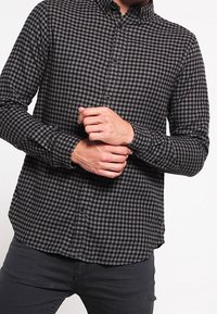 Musta- ja harmaaruutuinen pitkähihainen paita, jossa on napillinen kaulus. Paita on kapealahkeinen ja siinä on rakenteeltaan teksturoitu kangas.