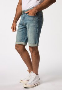 Pantalones cortos de denim en un azul claro con un acabado desgastado, puños doblados y un diseño clásico de cinco bolsillos. Se llevan con zapatillas altas blancas.