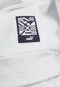 Tessuto bianco con spruzzi multicolori, messo in risalto da un rettangolo nero con motivi geometrici bianchi e il logo Puma.