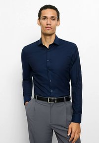 Marineblaues Langarmhemd aus glattem Stoff mit durchgehender Knopfleiste und kontrastierenden Manschetten, kombiniert mit grauer Hose und schwarzem Gürtel.