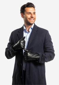 Schwarze Lederhandschuhe mit strukturierten Nähten, getragen von einem Mann in einem marineblauen Mantel über einem hellblauen gestreiften Hemd.