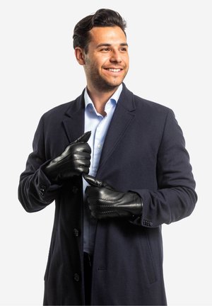 Schwarze Lederhandschuhe mit strukturierten Nähten, getragen von einem Mann in einem marineblauen Mantel über einem hellblauen gestreiften Hemd.