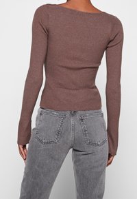 Brun ribbad långärmad topp med rundad halsringning, kombinerad med grå denim jeans med hög midja och klassisk 5-ficksdesign.