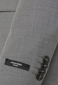 Szara teksturowana rękaw kurtki z czterema czarnymi guzikami i metką z napisem "JACK & JONES PREMIUM". Prosty, dopasowany fason.