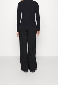 Mustapaita pitkillä hihoilla yhdistettynä löysiin mustiin housuihin. Paita on istuva malli, kun taas housut ovat leveälahkeiset ja sileäpintaiset.