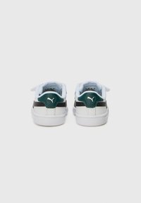 Sneakers featuring a white synthetic upper, black leather accents, and green heel tab. Velcro strap across the tongue for secure fit.