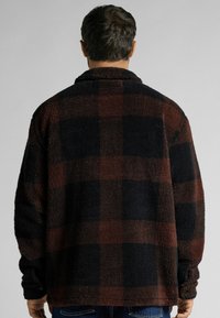 Överdimensionerad fleece skjortjacka i mörk marinblå och rödbrun rutigt mönster. Har krage, långa ärmar och en mjuk, strukturerad yta.