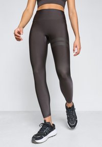 Kõrge vöökoht, mustad legginsid, millel on sile ja läikiv tekstuur, sisaldavad kahte horisontaalset triibu aktsenti reie peal ja on hästi nahakujulised.