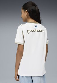 T-shirt bianco a maniche corte con accenti beige, con il logo "goodhabitz" sul retro e un badge sulla parte superiore sinistra. Tessuto testurizzato.