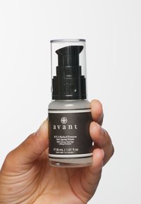 Siero anti-invecchiamento in una bottiglia trasparente con pompa e coperchio nero. La bottiglia ha un'etichetta grigia con testo bianco e un logo circolare.