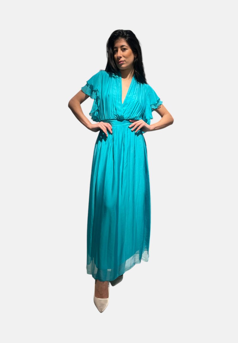 Abito maxi turchese con maniche a volant, vita cintrata e tessuto fluido, abbinato a scarpe col tacco beige.