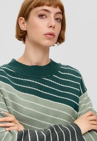 Gestreepte trui in groene en grijze tinten, met een geribbelde ronde hals en een zachte gebreide textuur. Opvallende witte diagonale strepen.