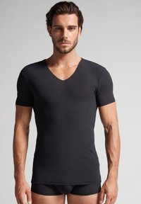 Černé tričko s krátkým rukávem ve tvaru V z hladkého materiálu, přiléhavý design, bezšvový lem, s těsným střihem a bez vzorů.