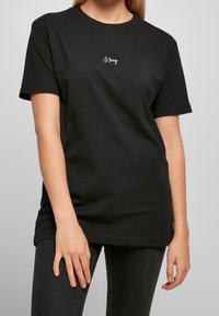 Černé bavlněné tričko s krátkými rukávy, kulatým výstřihem a bílou výšivkou "Merry" na hrudi. Měkká textura, uvolněný střih.