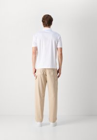 Camisa polo branca de manga curta combinada com calças cargo bege com múltiplos bolsos, usada com ténis brancos, vista de trás.
