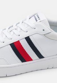 Białe sneakersy z gładkiej skóry, z czerwonymi i granatowymi paskami. Teksturowany język i plastikowe oczka z białymi sznurówkami. Wytrzymała gumowa podeszwa.