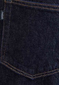 Donkerblauwe denim stof met een subtiele structuur. Heeft een schuin zakje met oranje stiksels en een klein merketiket aan de zijkant.