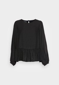 Blouse noire à manches longues avec de subtils pois, encolure ronde, détail en forme de trou de serrure au dos, et ourlet volanté sur un fond clair.