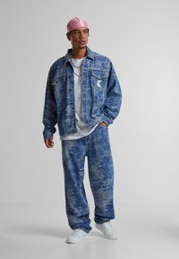 Blue denim jacket with a light wash, patterned pants in matching tones, and white sneakers. Features a pink headband and silver chain.