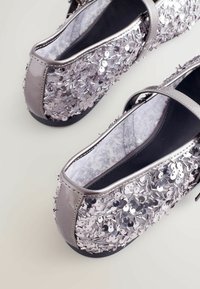 Silberne Ballerinas mit glitzernden Verzierungen, runder Spitze und einem glatten lederähnlichen Finish. Flache Sohle mit einem schlichten Riemendesign.