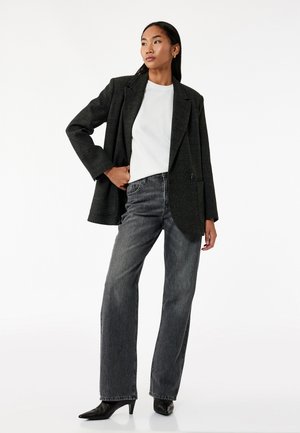 Donkergrijze blazer van een gestructureerde stof, witte crew-neck shirt en rechte zwarte jeans. Model draagt spitse zwarte hakken.