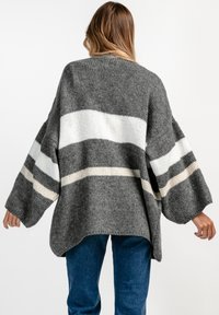 Szary, oversize sweter z białymi i kremowymi poziomymi paskami, o dzianinowej fakturze i szerokich rękawach. Stylizowany z dżinsowymi spodniami.